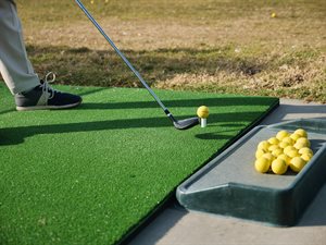 Photo of person holding golf club next to a ball on driving range